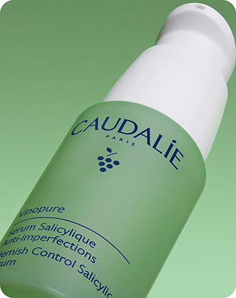 A green bottle of Caudalie Vinopure Blemish Control Salicylic Serum against a gradient green background.